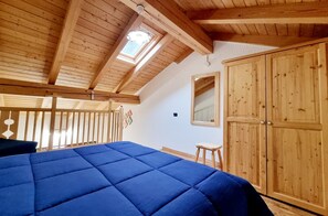 A bedroom with a wooden ceiling, a skylight, a large bed with a blue cover, and a wardrobe.