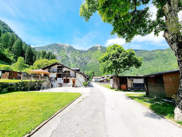 A rural village with traditional wooden houses, a paved road, and mountains in the background.