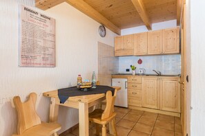 A wooden dining table with chairs, a small refrigerator, wooden cabinets, a clock, and a welcome sign with amenities listed. - Beautiful 'Adamello 15' Apartment with Wi-Fi (Pinzolo)