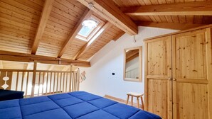 A bedroom with a wooden ceiling, a skylight, a large bed with a blue cover, and a wardrobe. - Beautiful 'Adamello 15' Apartment with Wi-Fi (Pinzolo)