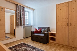 A room with a wooden floor, a sofa with cushions, a mirror, a wardrobe, and a radiator.