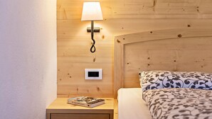 A wooden-paneled wall with a bedside lamp, a thermostat, and a book on a nightstand. - Cosy Apartment "Confolia 1" with Wi-Fi and Mountain View (La Valle)