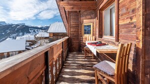 A wooden cabin with a balcony, a table with a red tray, and a chair. - Cosy Apartment "Confolia 1" with Wi-Fi and Mountain View (La Valle)