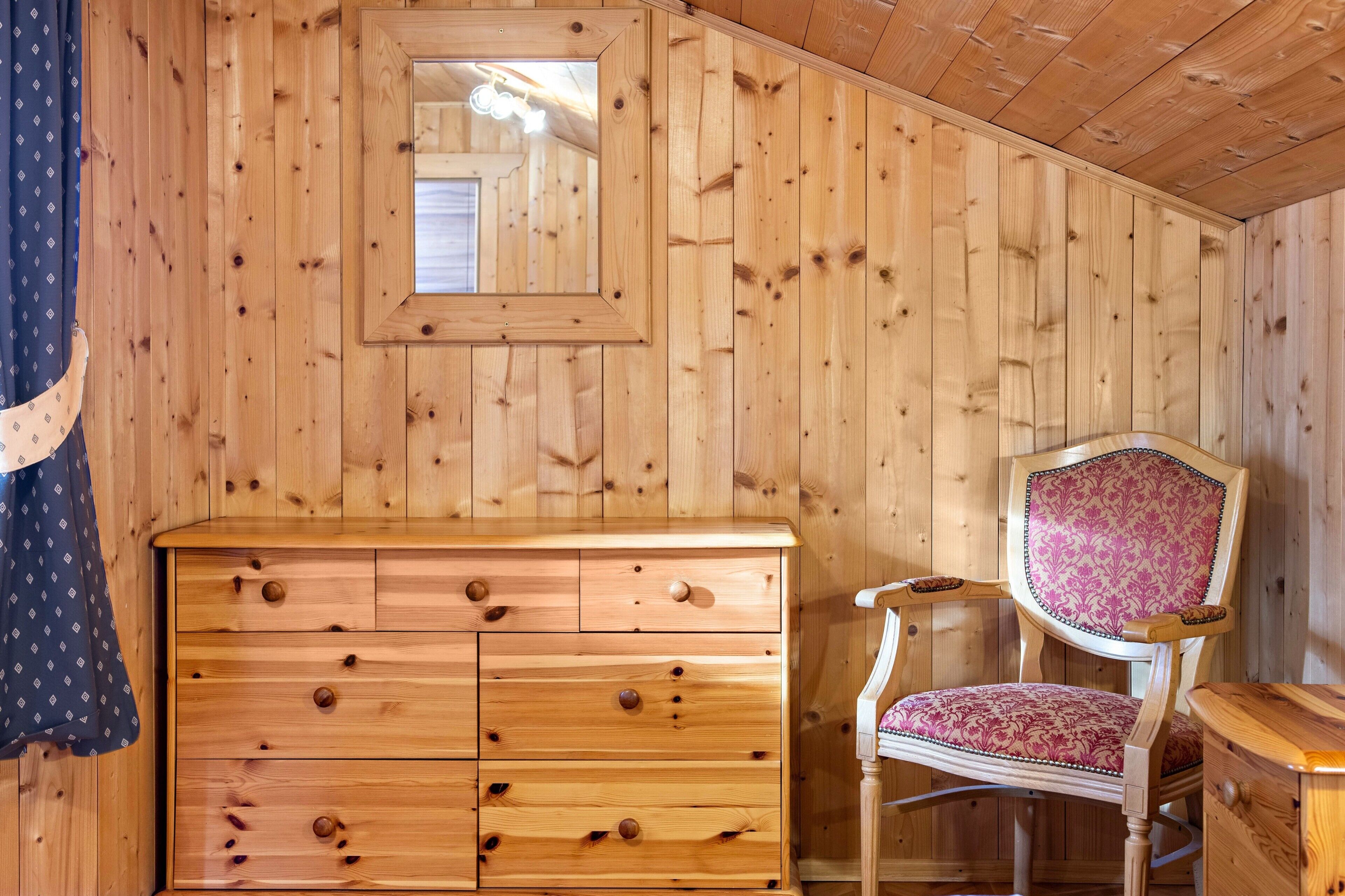 L’intérieur d’une cabane en bois, avec une commode, une chaise et un miroir.
