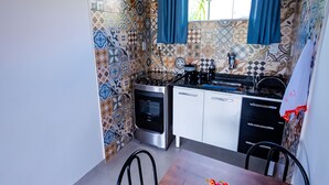 A compact kitchen with a stove, sink, and cabinets, a dining table with chairs, and a hanging pendant light. - Apartment furnished with air Penedo RJ (Jardim das Rosas)