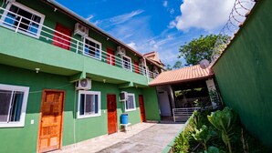 A two-story building with a green exterior, red doors, and white railings. - Apartment furnished with air Penedo RJ (Jardim das Rosas)