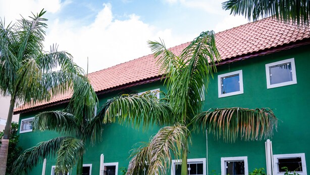 A green building with a red-tiled roof and multiple windows. - Apartment furnished with air Penedo RJ (Jardim das Rosas)