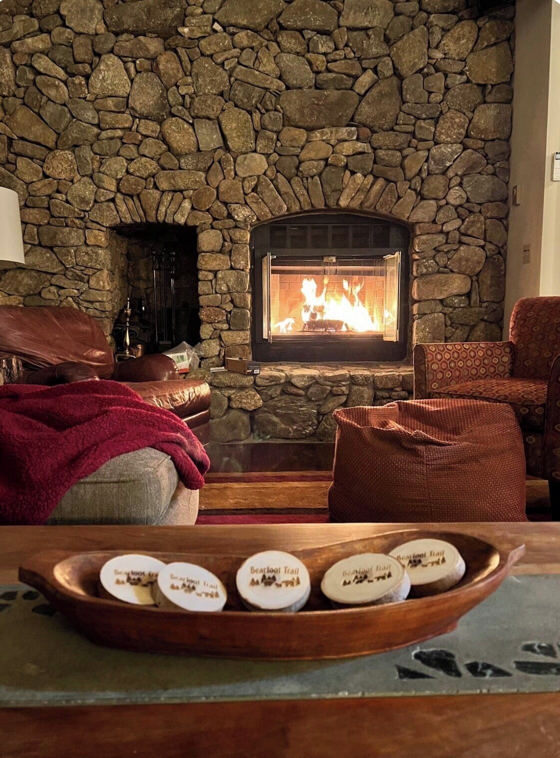 Una chimenea de piedra con fuego, un sillón de cuero, un sillón estampado y una bandeja con velas.