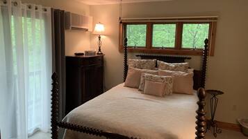 Quarto com cama de dossel, luminária de cabeceira, janela com vista para o verde e ventilador de teto.
