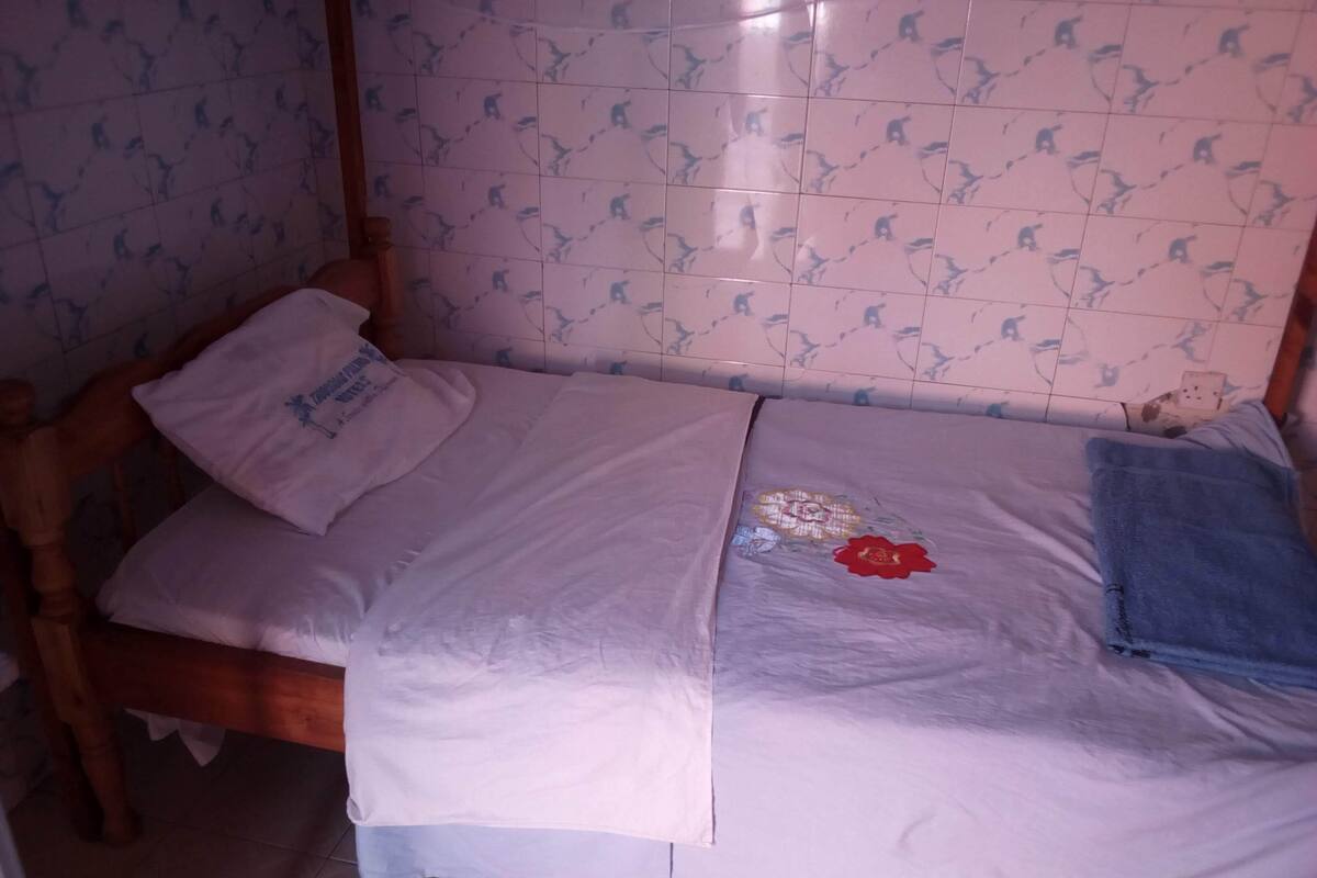 A small, single-bed room with a wooden headboard, a white bedspread, and a floral design on the bed.