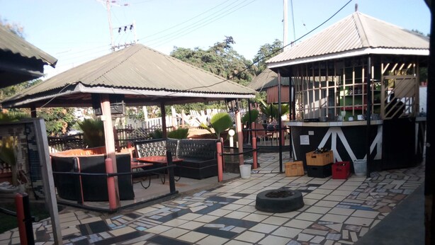 A covered outdoor seating area with tables and chairs, a tiled floor, and a small trash bin.