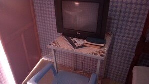 A small room with a television on a stand, a blue plastic chair, and patterned wallpaper.