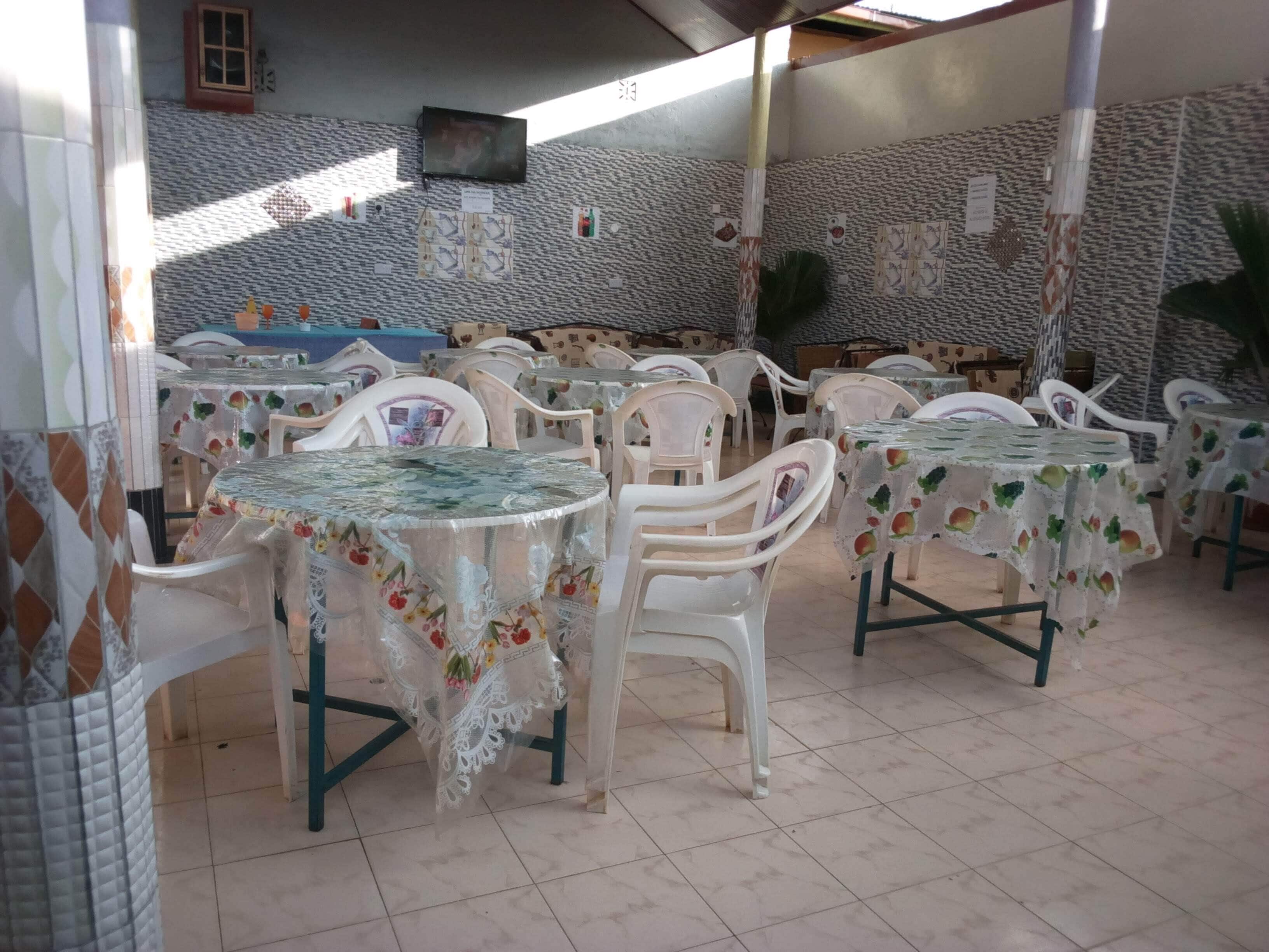 An outdoor dining area with multiple tables and chairs, a television mounted on the wall, and a tiled floor.