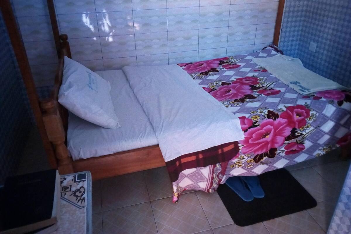 A small, single-bed room with a wooden frame, a floral bedspread, and a white pillow.