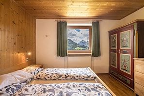 Una habitación con paredes de madera, una cama con ropa de cama estampada, una ventana con cortinas y un mueble con diseños florales.