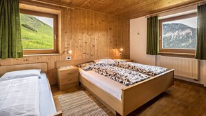 Et soveværelse med træpaneler, to senge, et natbord, et vindue med udsigt over et grønt landskab og en radiator.
