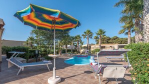 Un área de piscina con sillas de descanso y un paraguas de colores.
