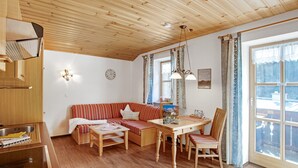 A cozy room with a wooden ceiling, a dining table with chairs, a sofa, and a window with curtains.