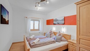 A bedroom with a wooden bed, a window with curtains, a wall-mounted light, and a painting.
