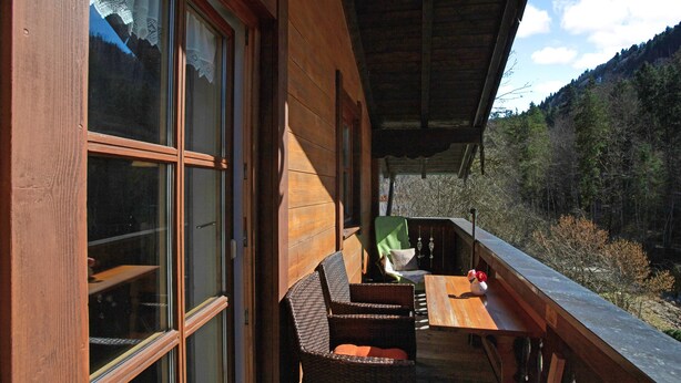 A wooden cabin with large windows, a wooden deck, and a view of a forested valley.
