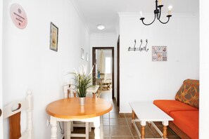 A dining area with a table and chairs, a potted plant, a white sofa, and a chandelier.