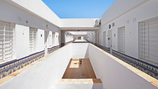 A long corridor with white walls, tiled flooring, and a central open space.
