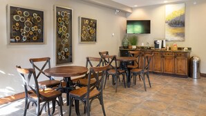 A dining area with round wooden tables and metal chairs, a kitchen with wooden cabinets, and artwork on the walls.