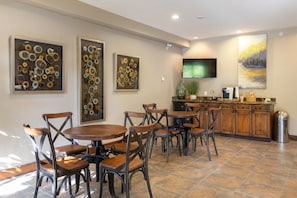 A dining area with round wooden tables and metal chairs, a kitchen with wooden cabinets, and artwork on the walls. - Great Location in Breck, Walk to Main Street! Private Hot Tub and Fireplace (Breckenridge)