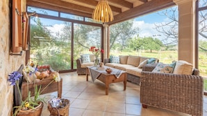 A spacious room with a large window, wicker furniture, a wooden ceiling, and a hanging light fixture. - Majorcan Finca with Pool - Son Draguet (Porreres)