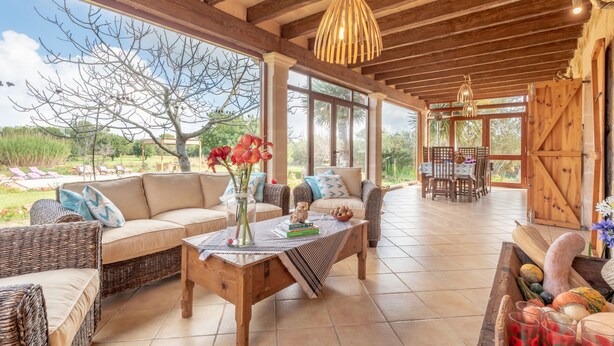 A spacious indoor area with a wooden ceiling, large windows, wicker furniture, and a dining area. - Majorcan Finca with Pool - Son Draguet (Porreres)