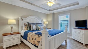 Un dormitorio con cama, mesitas de noche, cómoda, ventilador de techo y televisor.