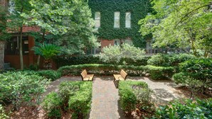 A garden courtyard with a paved walkway, two wooden benches, and a brick building with ivy-covered walls. - Heated Pool Access | 5*Clean | Flex Cancelation (Savannah)