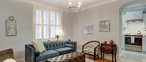 A living room with a blue sofa, a brown ottoman, a patterned rug, a wooden side table, and a chandelier.