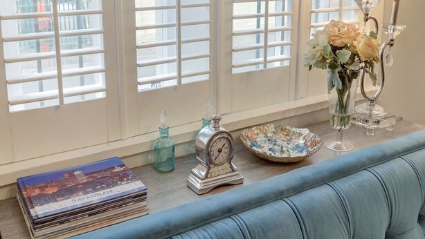 A room with a blue sofa, a stack of books, a decorative clock, a vase with flowers, and a candle holder. - Heated Pool Access | 5*Clean | Flex Cancelation (Savannah)