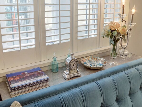 A room with a blue sofa, a stack of books, a decorative clock, a vase with flowers, and a candle holder. - Heated Pool Access | 5*Clean | Flex Cancelation (Savannah)