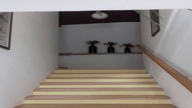 Een trap met houten treden en een leuning, die uitkomt op een plateau met drie zwarte vazen en een klein plankje.