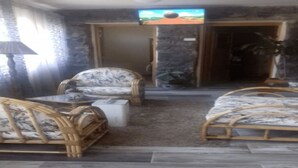 Een kamer met een bed, twee rieten stoelen, een tafeltje en een televisie aan de muur.
