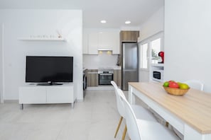 A modern kitchen with a TV, dining table, and a fruit bowl.