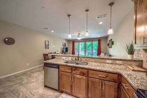 A kitchen with granite countertops, wooden cabinets, a dishwasher, and pendant lights.