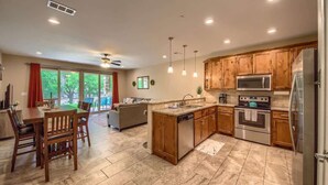 A modern kitchen with wooden cabinets, stainless steel appliances, and a dining area with a table and chairs. - RG 111 Guadalupe Fortress of Awesome (New Braunfels)