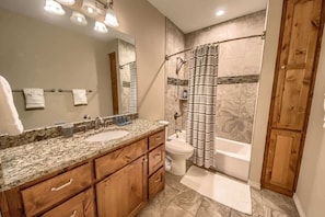 A bathroom with a double sink vanity, a shower with a striped curtain, and a toilet.