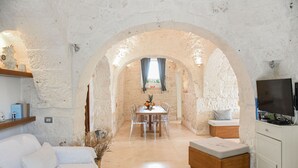 A rustic interior with a dining area, white sofa, and a television. - Luxury Villa "Trulli Terrarossa" in Apulian style with Pool (Martina Franca)