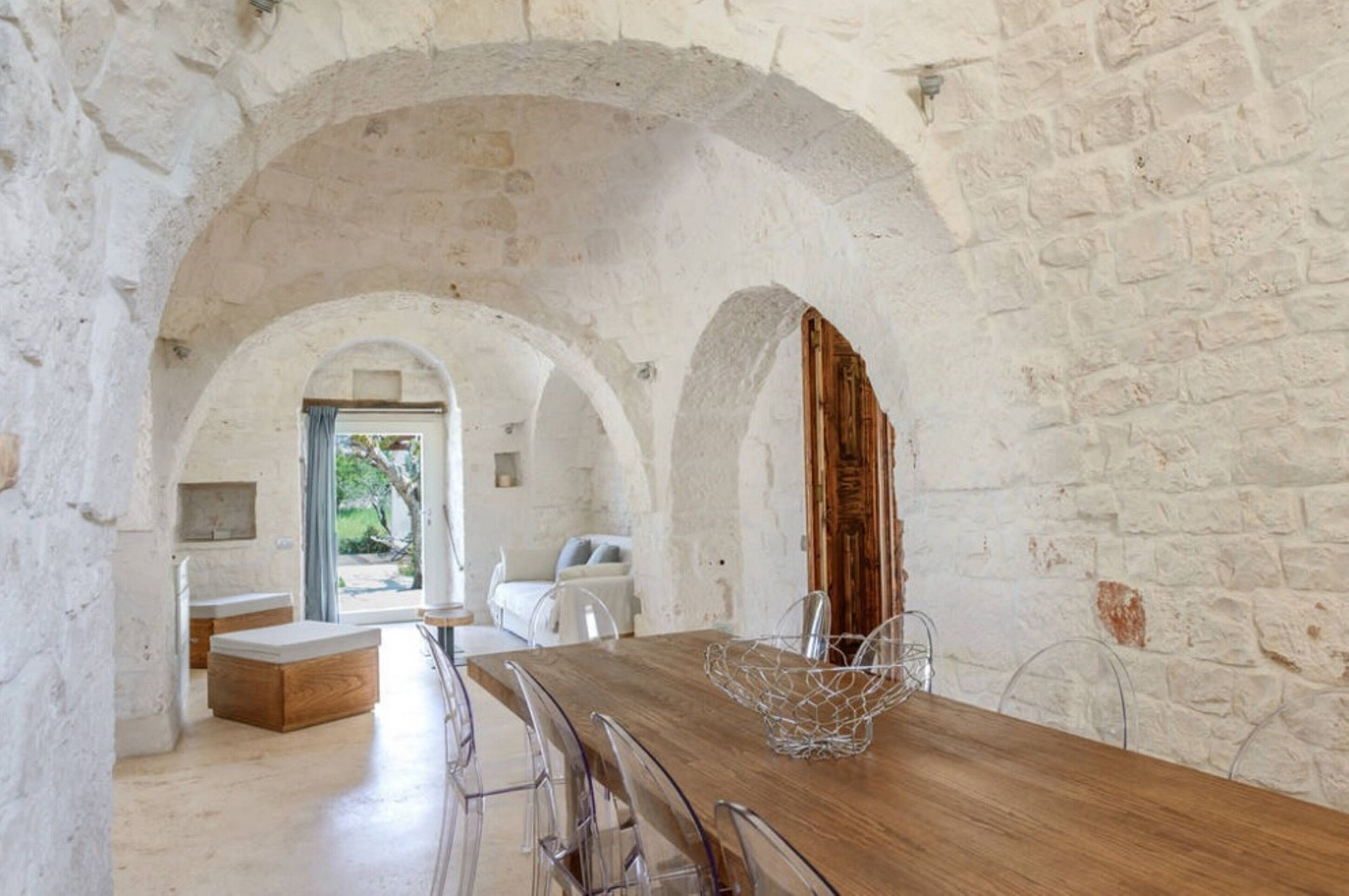 Un espace repas avec une table en bois, des chaises transparentes et un mur en pierre.