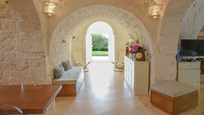 An interior with a stone archway, a sofa, a TV, and a view of greenery outside. - Luxury Villa "Trulli Terrarossa" in Apulian style with Pool (Martina Franca)