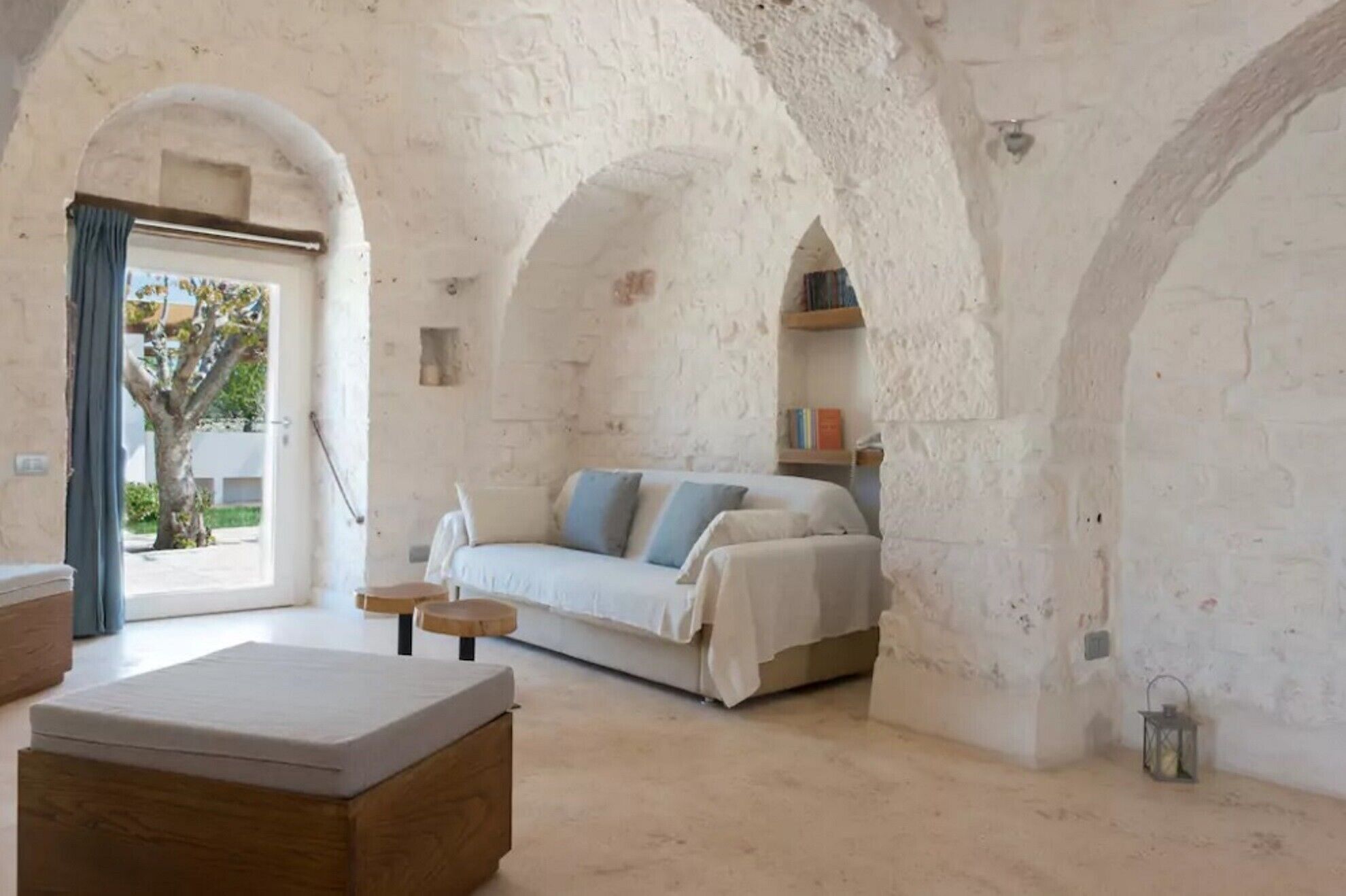 A room with a bed, a sofa, a small table, and a bench. There are bookshelves and a lantern on the walls.