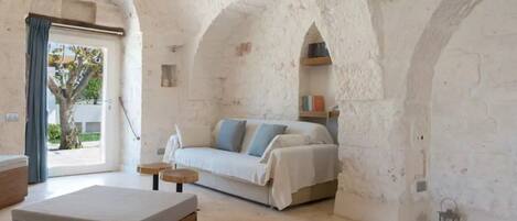 A room with a bed, a sofa, a small table, and a bench. There are bookshelves and a lantern on the walls.
