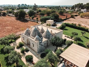 A stone building with multiple conical roofs, surrounded by greenery and open fields.