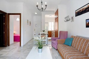 A living room with a sofa, a coffee table with a plant, a chandelier, and a dining area in the background.