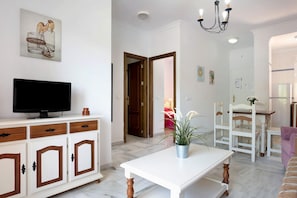 A living room with a television on a cabinet, a dining area with a table and chairs, and a kitchen in the background.