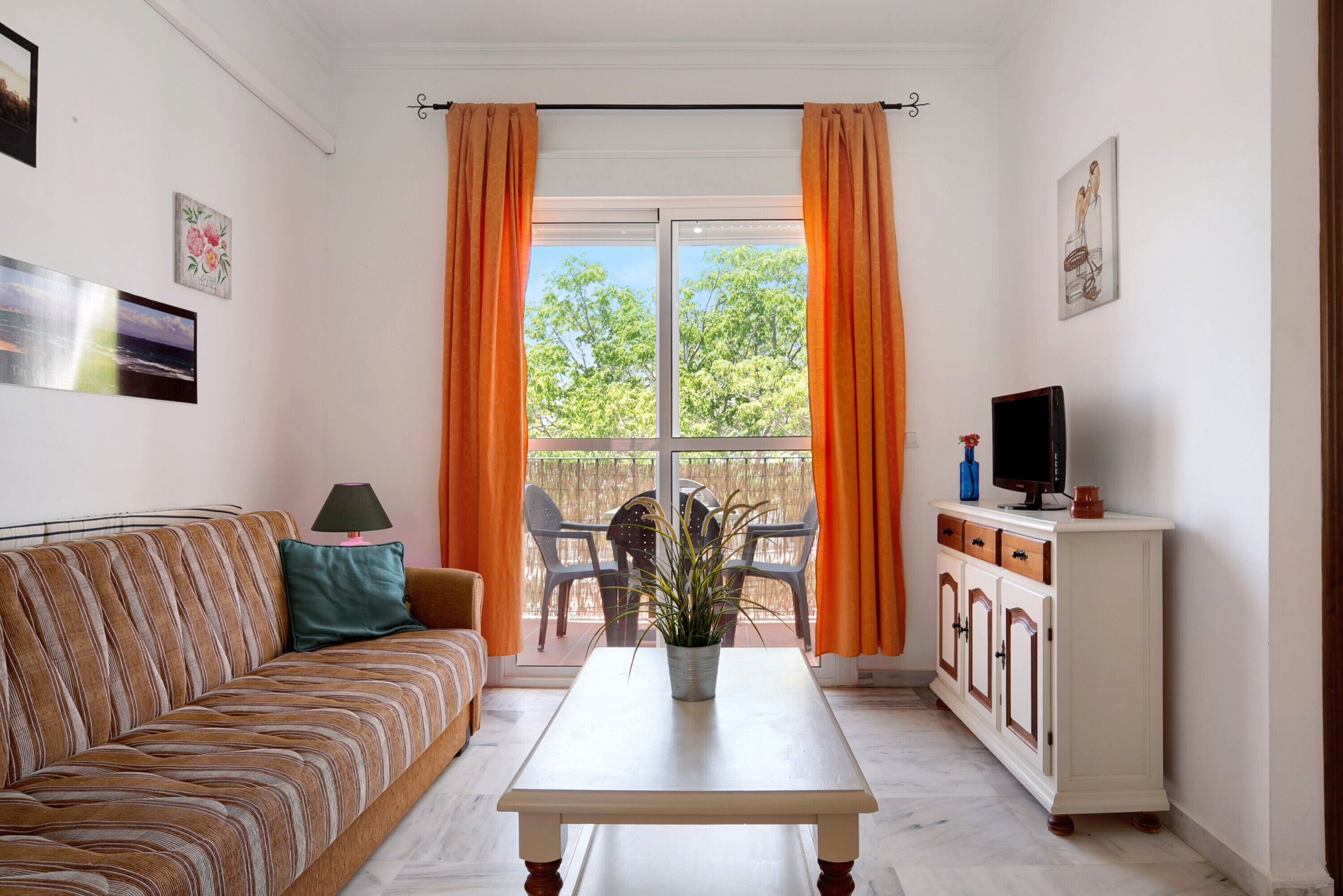 Una habitación con sofá, mesa, armario, televisor y ventana con cortinas.